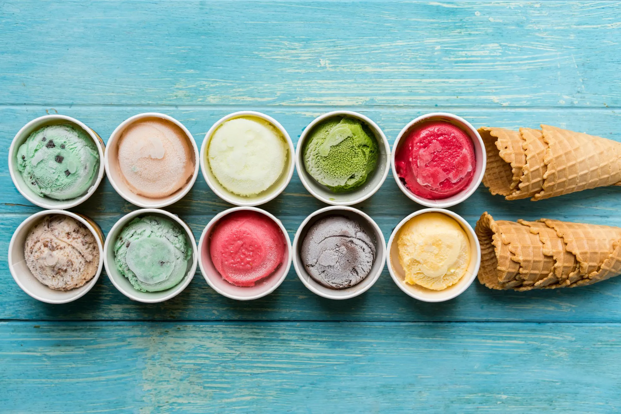 Tubs of colorful ice cream flavors next to waffle cones